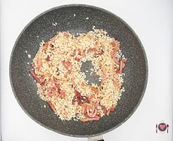 La foto raffigurante l'aggiunta di riso per la preparazione del Risotto zafferano e speck
