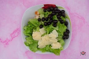La foto raffigurante l'insalata spezzata e aggiunta nella zuppiera assieme ai petali di Grana e olive per la preparazione dell'insalata di pollo